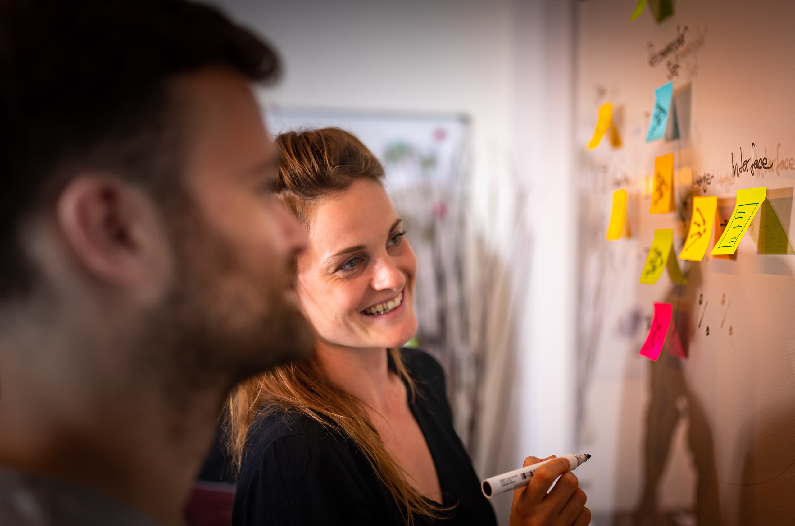 Zwei Limebit Mitarbeiter:innen kleben bei einem Workshop Notizzettel an eine Tafel.
